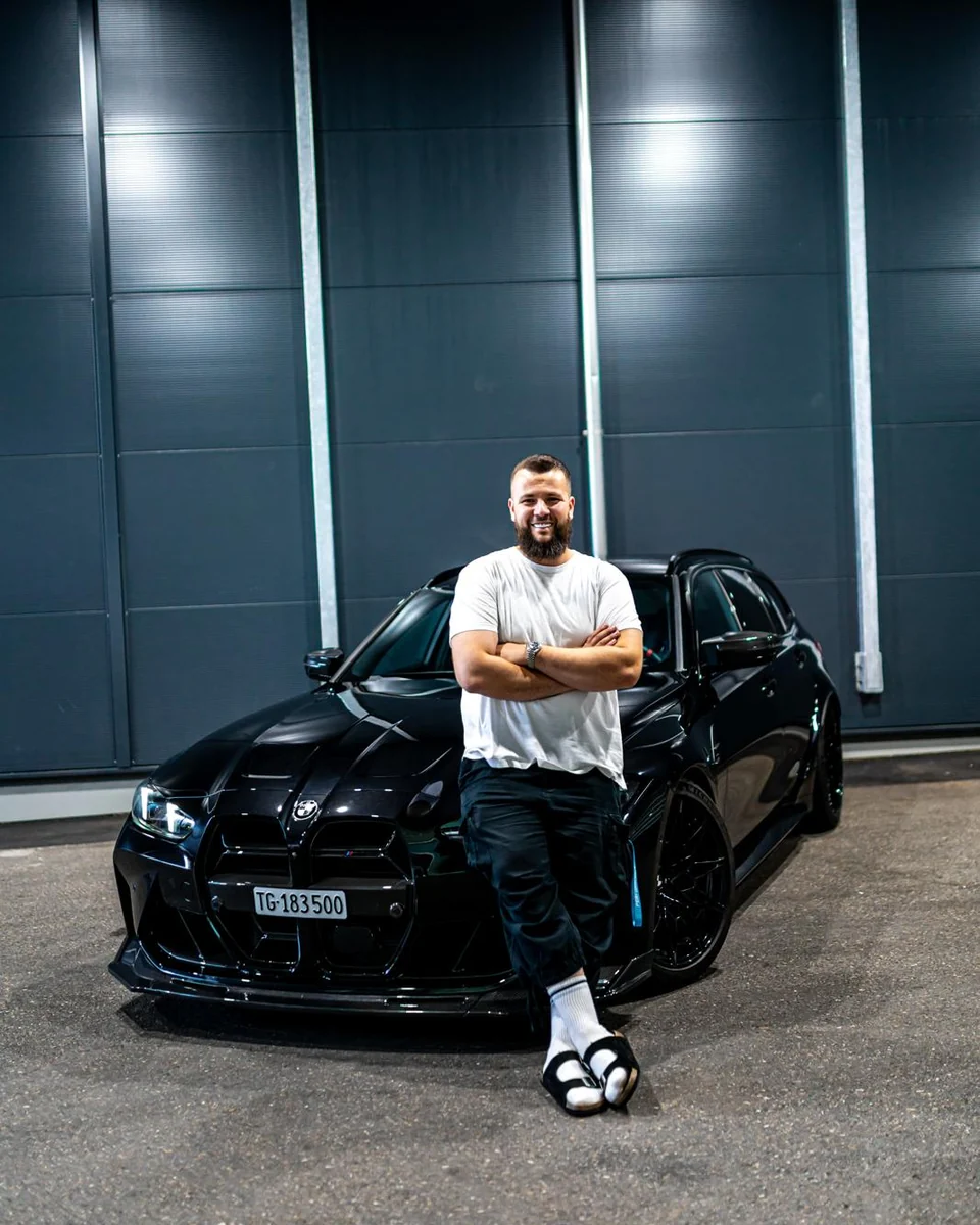 Ardian Fetahu, angelehnt an einen schwarzen BMW vor der Halle